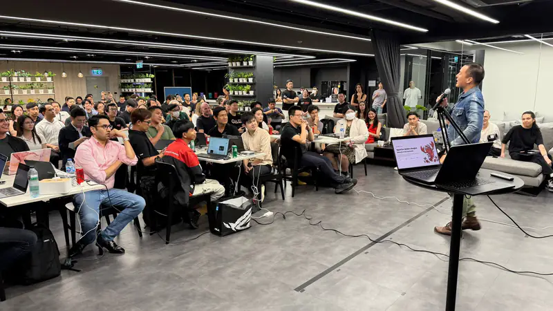 A speaker presents to a full room of builders with laptops